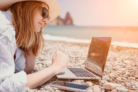 Woman sea laptop. Business woman in yellow hat working on laptop by sea. Close up on hands of pretty lady typing on computer outdoors summer day. Freelance, digital nomad, travel and holidays concept