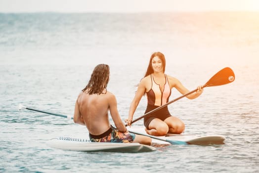 Sea woman and man on sup. Silhouette of happy young woman and man, surfing on SUP board, confident paddling through water surface. Idyllic sunset. Active lifestyle at sea or river