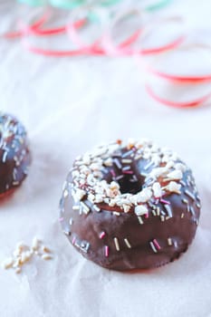 Sweet chocolate donut with sprinkles and party decorations on light background, Delicious colorful chocolate donut. Vertical