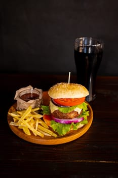 Delicious hamburger with cola and potato fries on a wooden table with a dark brown background behind. Fast food concept. High quality photo