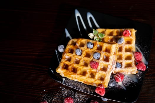 Belgian French waffles close-up with berries, blueberries athens raspberries blueberries sprinkled with powdered sugar, condensed milk, side view isolated on black background. Sweet breakfast dessert