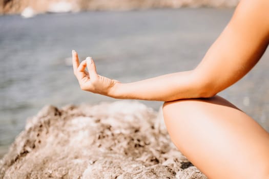 Yoga on the beach. A happy woman meditating in a yoga pose on the beach, surrounded by the ocean and rock mountains, promoting a healthy lifestyle outdoors in nature, and inspiring fitness concept