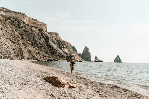 Woman beach vacation photo. A happy tourist in a blue bikini enjoying the scenic view of the sea and volcanic mountains while taking pictures to capture the memories of her travel adventure