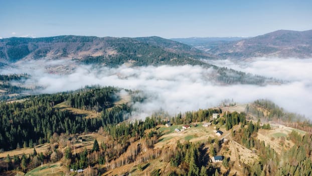 Mountains in clouds at sunrise in spring. Aerial view of mountains with green trees in fog. Beautiful landscape with hills, forest, sky. Top view from drone of mountain valley in low clouds