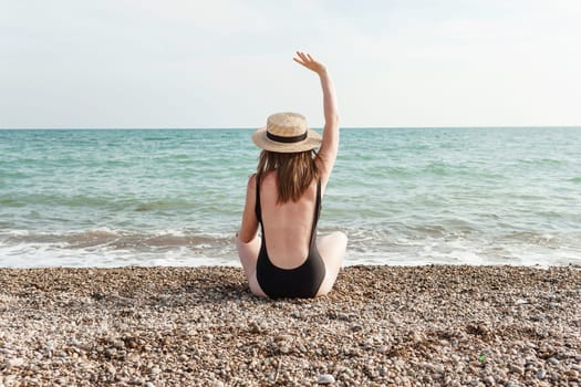 Woman in black swimsuit and straw hat on beach, seaside. View from the back. Summer vacation at the sea