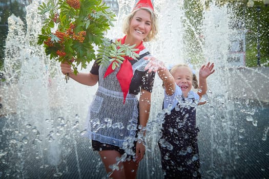 Young and adult schoolgirl on September with flowers having fun near water of fontain. Generations of schoolchildren, pioneer of USSR and October girl in modern uniform of Russia. Mom and daughter