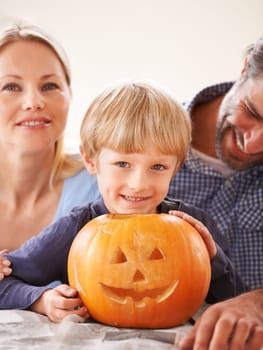 Family, portrait and parents of kid with pumpkin to celebrate halloween, fun and creativity at home. Happy boy child, mom or dad carving face in orange vegetable, holiday lantern and party decoration.