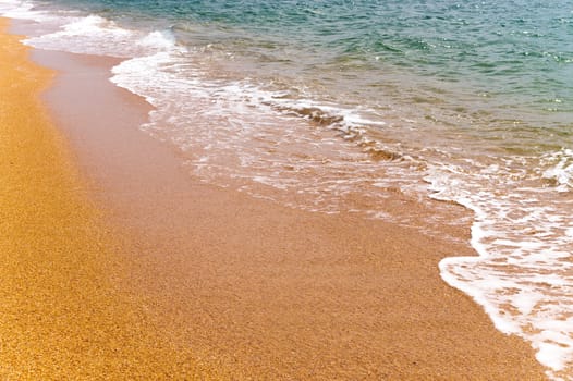 Close-up, calm ocean or sea surf crashing onto a golden sandy beach.