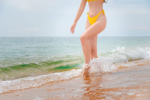 young woman walking along the beach, close-up. a girl cheerfully walks into the sea with waves with a golden sandy beach along the coast.
