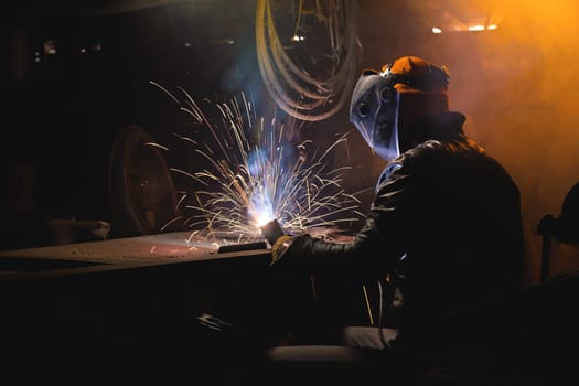 a man working with an electric welding machine. a man in safety glasses and a leather jacket cooks spare parts in his garage.