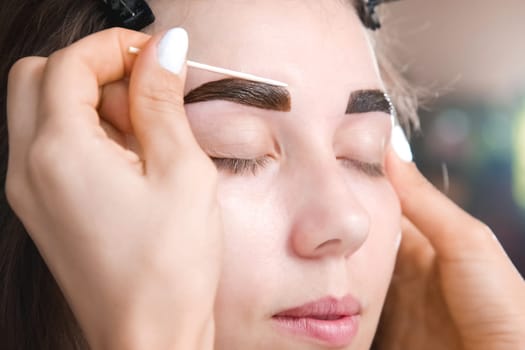 Eyebrow tinting. Close-up of a technician applying eyebrow dye or removing excess paint. Cosmetic procedures, eyebrow makeup in a beauty salon by a professional.