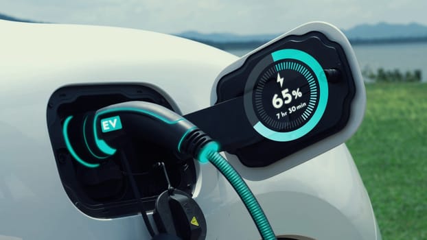 Electric car plug in with charging station, recharge battery by EV charger cable display smart digital battery status hologram with nature background. Futuristic green energy infrastructure.Peruse