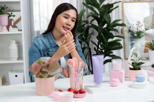 Young beautiful Asian girl reviewing moisturizing body lotion cream product to make glow skin testing on arm on social media online live recording smartphone with bestseller at modern room. Stratagem.