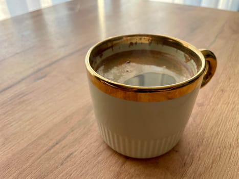 Morning coffee in a green cup with a golden rim stands on a wooden table. High quality photo