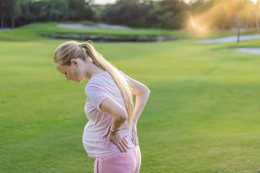 Expectant woman experiences back pain outdoors, seeking relief and comfort during pregnancy with a gentle outdoor stretch or rest.