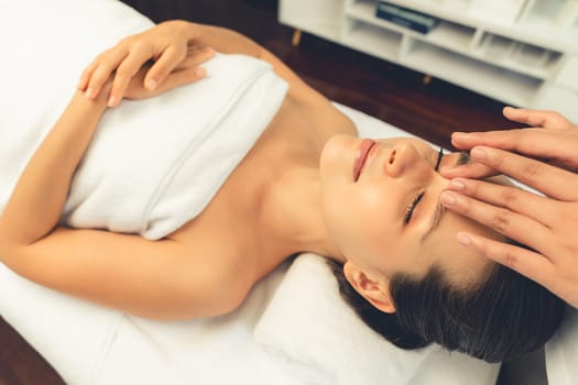 Caucasian woman enjoying relaxing anti-stress head massage and pampering facial beauty skin recreation leisure in dayspa modern light ambient at luxury resort or hotel spa salon. Quiescent