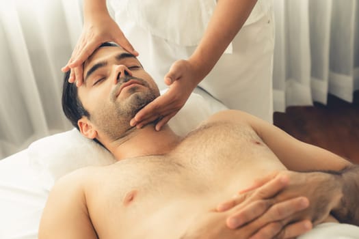 Caucasian man enjoying relaxing anti-stress head massage and pampering facial beauty skin recreation leisure in dayspa modern light ambient at luxury resort or hotel spa salon. Quiescent