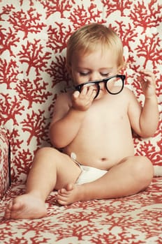 Glasses, playing and sweet baby in a studio with vision, health or eye care accessory for development. Cute, eyewear and young child, infant or toddler kid with spectacles by wallpaper background