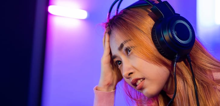 Game Over. Asian gamer playing online video game she losing and sad on computer PC colorful neon LED lights, young woman in gaming headphones feeling disappointed about lost game, E-Sport concept