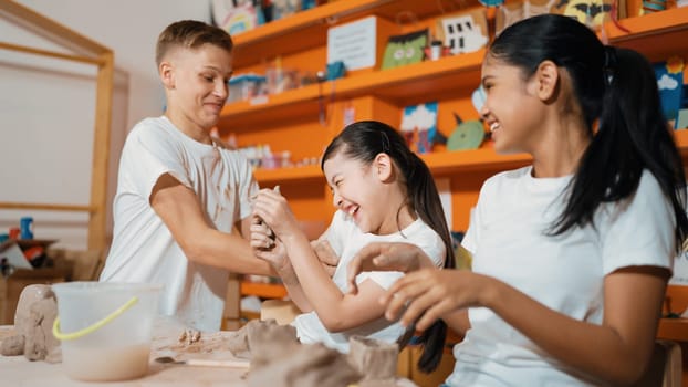 Handsome student playing with friend while put the clay on shirt at class. Group of diverse children working or modeling vase. Happy boy put water to young girl while laugh with happy. Edification.