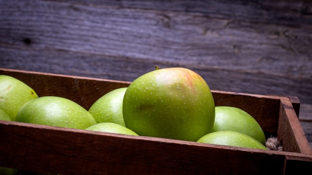 Wooden crate with ripe green apples on wooden table.