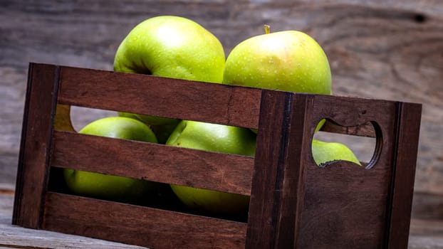 Wooden crate with ripe green apples on wooden table.