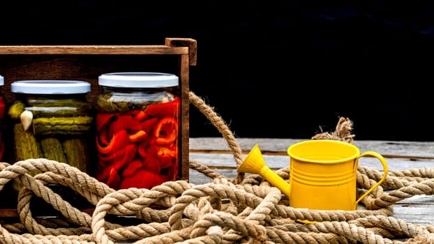 Wooden crate with glass jars with pickled red bell peppers and pickled cucumbers (pickles) isolated. Jars with variety of pickled vegetables. Preserved food concept in a rustic composition.