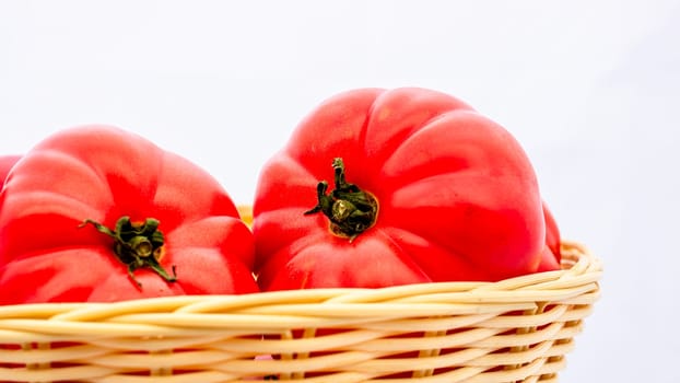 Fresh and tasty red tomatoes in wicker basket isolated