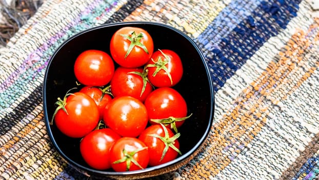 Detail of ripe cherry tomatoes in small black bowl on a rustic napkin. Ingredients and food concept