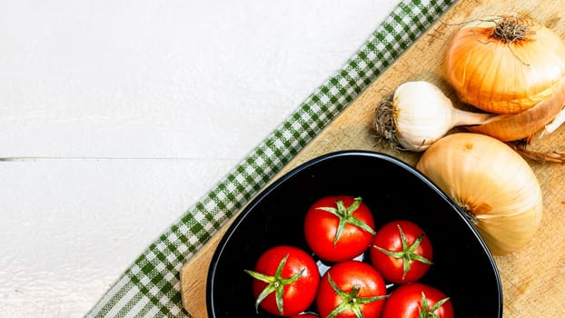 Top view of onions, garlic and fresh ripe cherry tomatoes on a rustic white wooden table. Ingredients and food concept