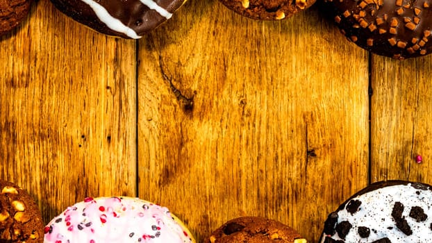 Colorful donuts on wooden table. Sweet icing sugar food with glazed sprinkles, doughnut with chocolate frosting. Top view with copy space