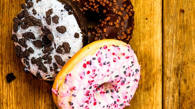 Colorful donuts on wooden table. Sweet icing sugar food with glazed sprinkles, doughnut with chocolate frosting. Top view with copy space