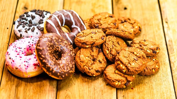 Colorful donuts and biscuits on wooden table. Sweet icing sugar food with glazed sprinkles, doughnut with chocolate frosting. Top view with copy space