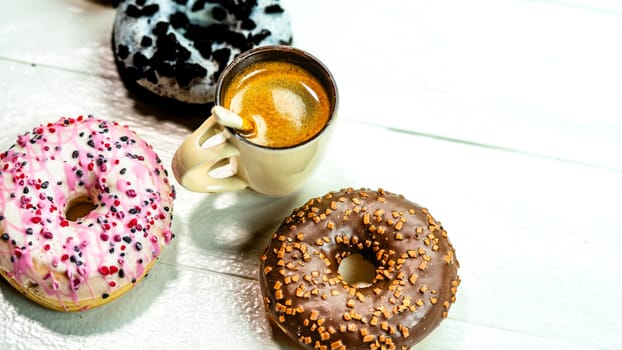 Colorful donuts and coffee cup on white wooden table. Sweet bakery with glazed sprinkles, breakfast concept. Top view with copy space