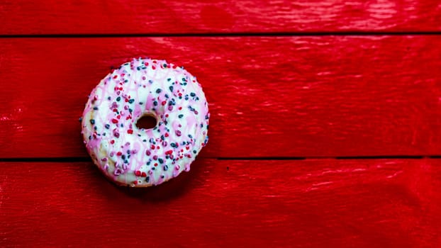 Colorful donuts on red wooden table. Sweet icing sugar food with glazed sprinkles, doughnut with chocolate frosting. Top view with copy space