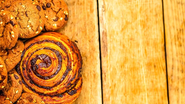 Colorful donuts, puff pastry and biscuits on wooden table. Sweet icing sugar food with glazed sprinkles, doughnut with chocolate frosting. Top view with copy space