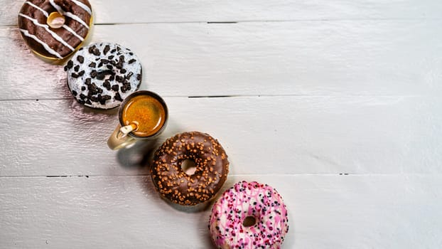 Colorful donuts on white wooden table. Sweet icing sugar food with glazed sprinkles, doughnut with frosting. Top view with copy space