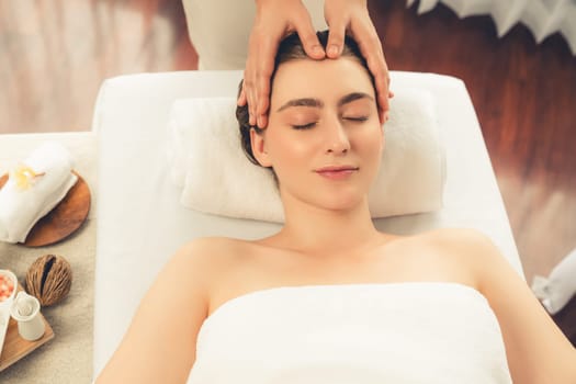 Caucasian woman enjoying relaxing anti-stress head massage and pampering facial beauty skin recreation leisure in dayspa modern light ambient at luxury resort or hotel spa salon. Quiescent