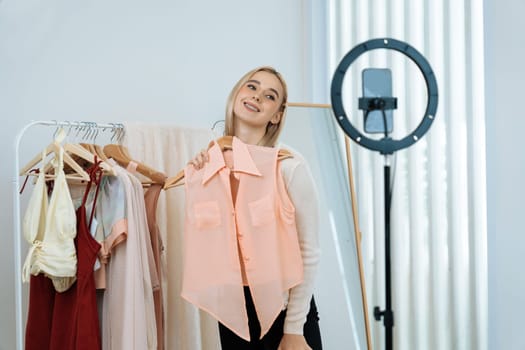 Young social medial content creator woman make fashion video. Blogger smiles to camera and light ring while making persuasive online clothing sell vlog to audience or follower. Blithe