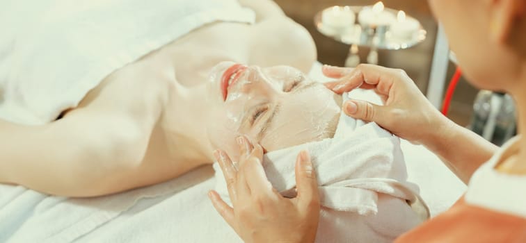 Portrait of beautiful caucasian woman having facial massage with homemade facial mask while lies on spa bed surrounded by beauty electrical equipment and peaceful nature environment. Tranquility.