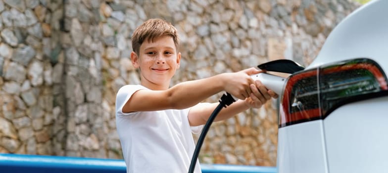 Little boy recharging eco-friendly electric car from EV charging station. EV car road trip travel concept for alternative transportation powered by clean renewable and sustainable energy. Perpetual