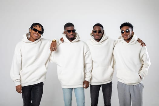 Group of African American guys in brown hoodies posing on a white background wearing sunglasses. High quality photo