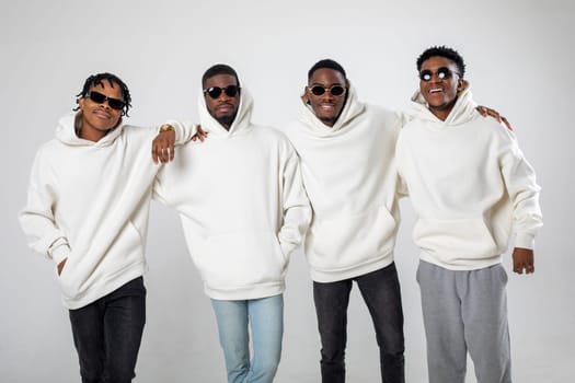 Group of African American guys in brown hoodies posing on a white background wearing sunglasses. High quality photo