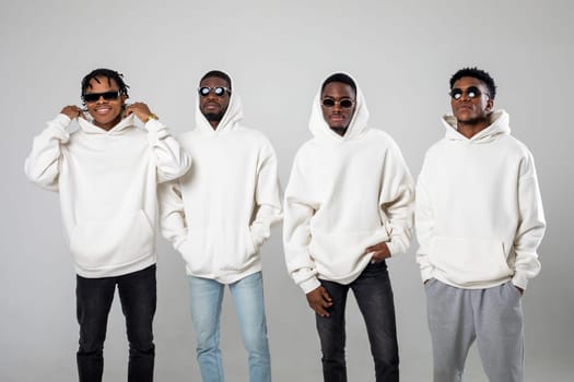 Group of African American guys in brown hoodies posing on a white background wearing sunglasses. High quality photo