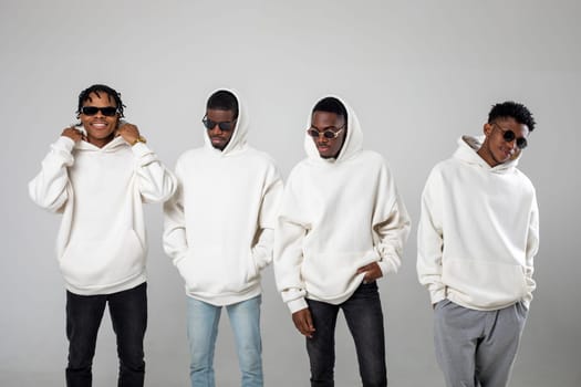 Group of African American guys in brown hoodies posing on a white background wearing sunglasses. High quality photo