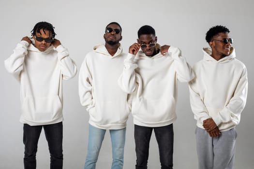 Group of African American guys in brown hoodies posing on a white background wearing sunglasses. High quality photo