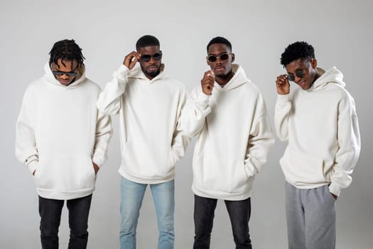 Group of African American guys in brown hoodies posing on a white background wearing sunglasses. High quality photo