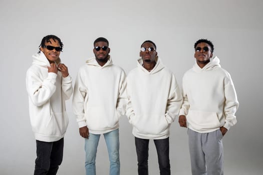 Group of African American guys in brown hoodies posing on a white background wearing sunglasses. High quality photo