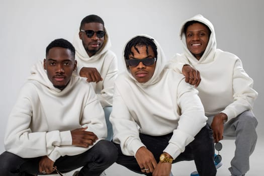 Group of African American guys in brown hoodies posing on a white background. Two in sunglasses. High quality photo