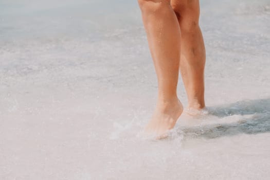 Sea beach travel - woman walking on sand beach leaving footprints in the white sand. Female legs walking along the seaside barefoot, close-up of the tanned legs of a girl coming out of the water